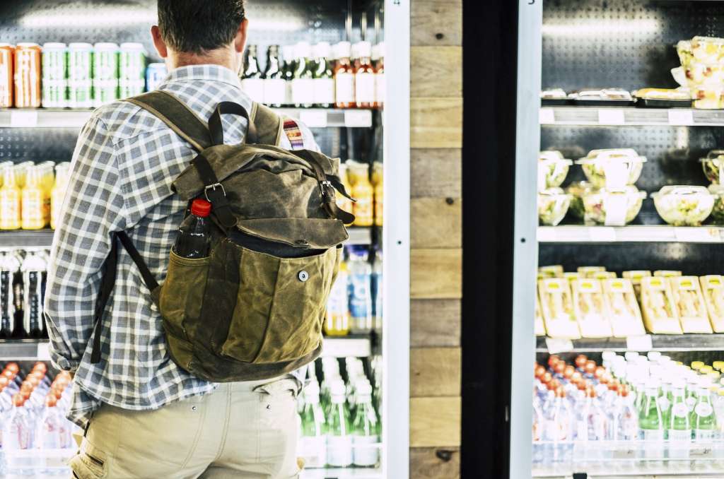 Rear view of man in backpack standing against cold drink beverage store. Man choosing drink